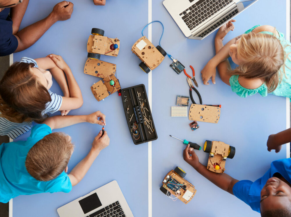 Group of children assembling technology kits with tools and electrical parts.