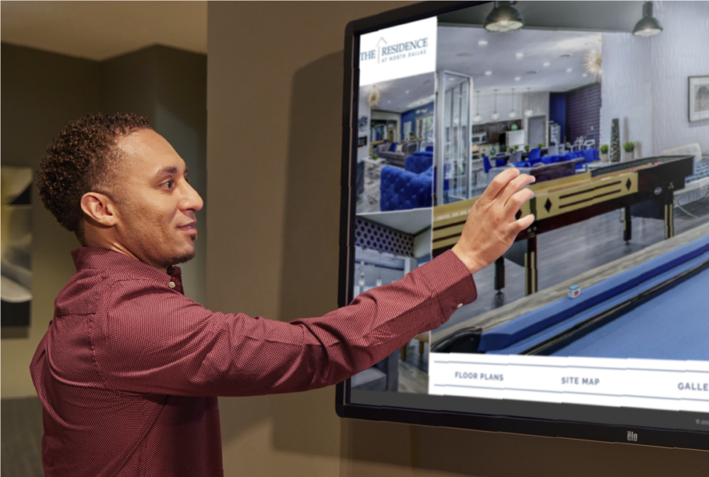 Person interacting with large wall mounted Touch Tour screen showing photos of property game room.
