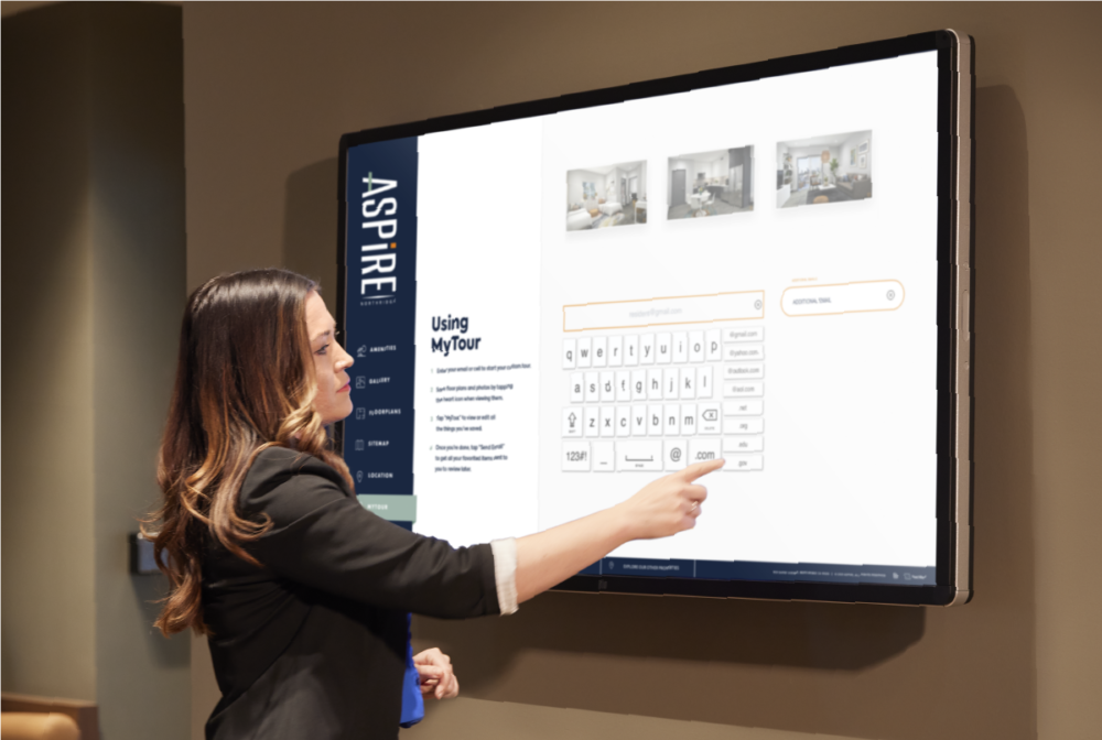 Person interacting with large wall mounted Touch Tour screen showing software interface and My Tour feature.
