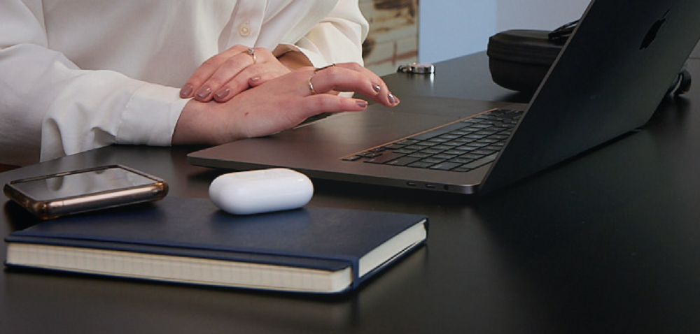Person working on laptop at desk with notebook, Air Pods headphones, and phone.