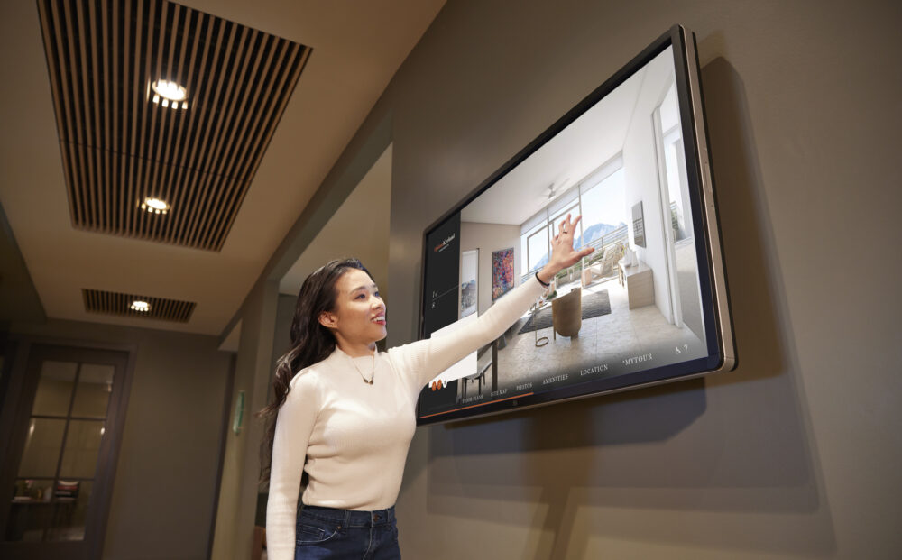 Person interacting with large wall mounted Touch Tour screen showing software interface with property photos.