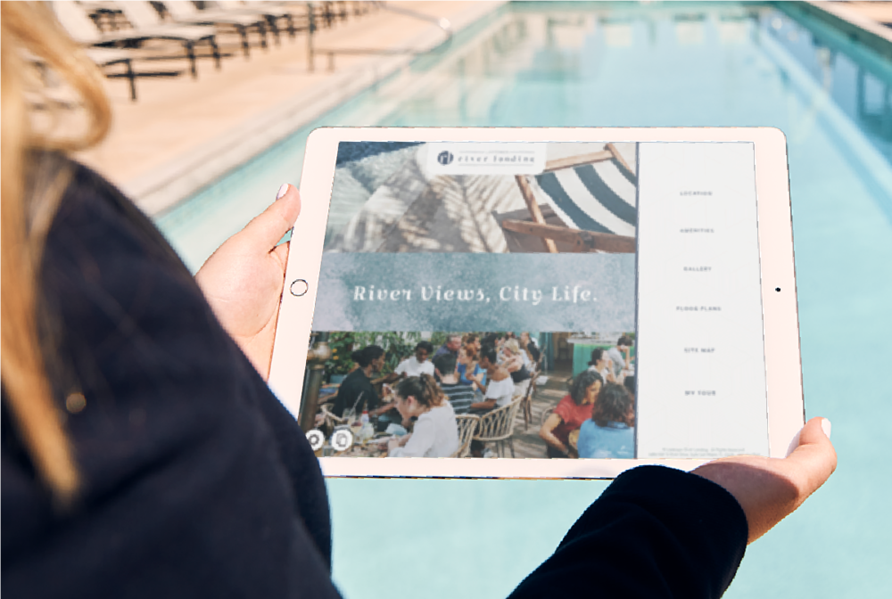 Person standing in front of sunlit pool holding iPad showing Touch Tour software interface with navigation and lifestyle photos.